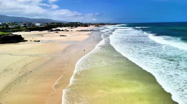 Huzurlu ve sakin bir sahil sahnesi sunar güzel altın kumlar ve canlı mavi gökyüzünün altında narin okyanus dalgaları