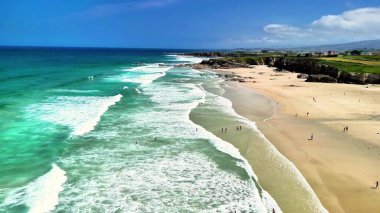 Nefes kesen kıyı manzaraları dalgaları, yumuşak kumları ve ufukta canlı mavi gökyüzünü gösteriyor.