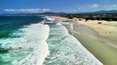 Dalgalar, altın kumlar ve açık mavi gökyüzüyle nefes kesici kumsal manzaralarının tadını çıkar.