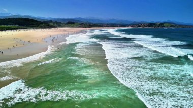 Dalgalar görkemli bir şekilde güneşli bir plaja çarpar neşeli ve kaygısız insanların çarpıcı güzel sahil şeridinin tadını çıkardıkları yere.