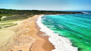 Yumuşak, ılık kumları, berrak gökyüzünün altında canlı mavi suların yanında gösteren nefes kesici bir kumsal sahnesi.