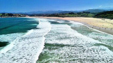 Hava manzaralı canlı dalgalar ve güneşin ve denizin tadını çıkaran neşeli insanların olduğu canlı bir sahil.