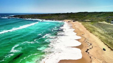 Canlı turkuaz dalgalar ve yumuşak altın kumlarla bezenmiş sakin bir sahili yakalayan çarpıcı bir hava manzarası.