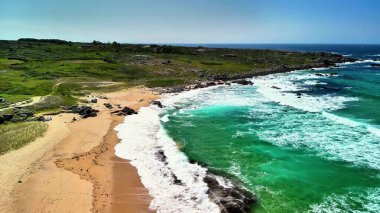 Sersemletici hava manzaraları sakin bir kıyı şeridini gösteriyor, canlı turkuaz suları vurguluyor ve yeşeren yeşillikler