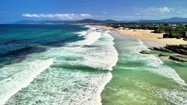 Altın kumlu kıyıya çarpan canlı dalgaların sergilendiği güzel sahilin çarpıcı hava manzarası.