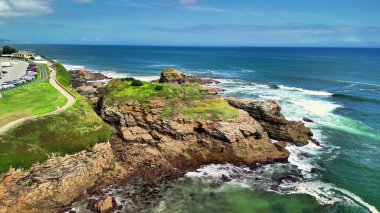 Dalgaların mavi gökyüzünün altındaki görkemli kayalıklara çarptığı kayalık bir kıyı şeridinin çarpıcı manzarasını deneyin.