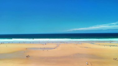 Güzel altın kumların, yumuşak dalgaların ve yukarıda parlak mavi gökyüzünün olduğu sakin kumsalın tadını çıkar.