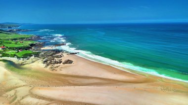 Göz kamaştırıcı hava manzarası güzel kumlu bir sahil ve canlı bir okyanus, arka planda yemyeşil tepeler