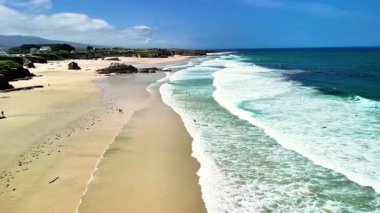 Nefes kesen manzaralı bir sahil manzarası yumuşak kumları, yumuşak dalgaları ve sakin gökyüzünü gösteriyor.