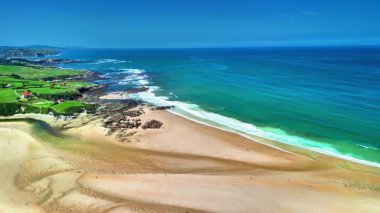 Göz kamaştırıcı hava manzarası güzel kumlu bir sahil ve canlı bir okyanus, arka planda yemyeşil tepeler