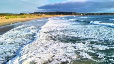 Gün batımında kumsala vuran yumuşak dalgaların nefes kesici manzarası, sahil güzelliğini vurguluyor..