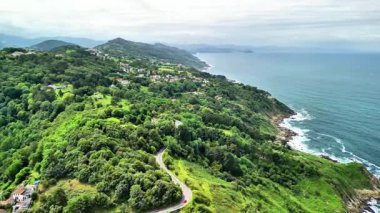 Göz kamaştırıcı bir hava manzarası, kıyı boyunca güzel dolambaçlı yolları olan canlı, yemyeşil bir kıyı şeridi sergiliyor.