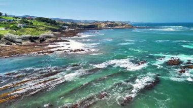 Hava çekimleri, turkuvaz suları ve çarpıcı manzaralı kaya oluşumlarının yer aldığı canlı bir kıyı şeridini güzel bir şekilde yakalıyor.