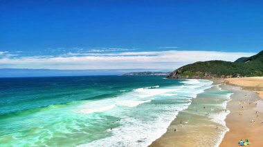Nefes kesici bir kumlu sahil manzarası. Titreyen dalgalar ve açık mavi gökyüzü.