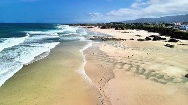 Nefes kesici bir hava manzarası, kumlu kıyılarda dalgalanan yumuşak dalgalarla çarpıcı bir kumsalın güzelliğini yakalar.
