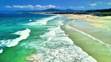 Turkuaz suları ve berrak mavi gökyüzünün altında hafif dalgalarla nefes kesici bir sahil manzarası..