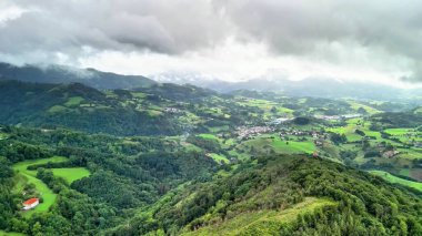 Yuvarlanan tepelerin nefes kesici kuş bakışı manzarası ve güzel, bulutlu bir gökyüzüne karşı kurulmuş canlı yeşillik.