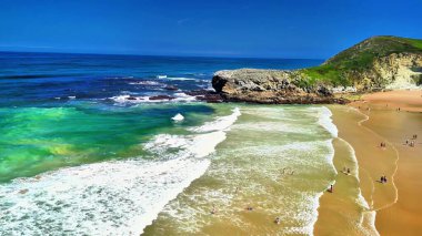 Bu, yakınlardaki manzaralı uçurumların yanında canlı turkuaz suların yer aldığı el değmemiş bir sahilin havadan çekilmiş görüntüsü.