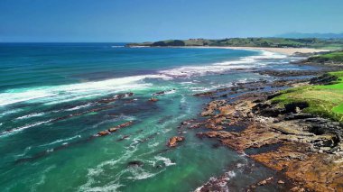 Temiz su, engebeli kayalar ve güneşli gökyüzünün altındaki yeşil tepeler ile güzel bir sahil manzarası, dinlenmek için ideal.