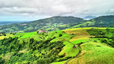 Güzel bulutlu gökyüzünün altında canlı yeşil tepeleri ve huzurlu manzaraları gösteren bir hava manzarası.