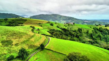 Göz kamaştırıcı bir hava manzarası, güzel, bulutlu gökyüzünün altındaki yemyeşil tepeleri gösteriyor, doğal güzellikler bakımından zengin.