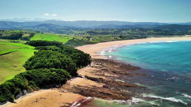 Yeşillik ve berrak mavi sulara karşı kumlu bir sahilin nefes kesici manzarası..