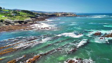 Hava çekimleri, turkuvaz suları ve çarpıcı manzaralı kaya oluşumlarının yer aldığı canlı bir kıyı şeridini güzel bir şekilde yakalıyor.