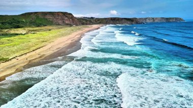 Bu çarpıcı hava görüntüsü sakin sahili ve berrak, parlak gökyüzünün altındaki canlı okyanus dalgalarını yakalar.