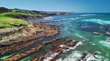 Berrak bir gökyüzü altında kayalık oluşumların ve canlı turkuaz suların yer aldığı nefes kesici kıyı manzaraları..