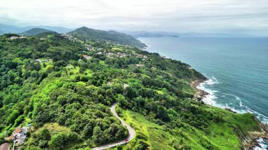 Göz kamaştırıcı bir hava manzarası, kıyı boyunca güzel dolambaçlı yolları olan canlı, yemyeşil bir kıyı şeridi sergiliyor.