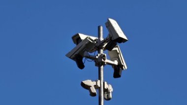 Stratejik olarak yüksek bir direğe yerleştirilmiş bir güvenlik kamerası koleksiyonu. Hepsi yukarıdaki gökyüzünü net bir şekilde görüyor.