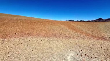 Göz kamaştırıcı ve büyüleyici kurak bir manzara berrak bulutsuz bir gökyüzünün altında canlı bir toprak rengi paleti ile dolu.