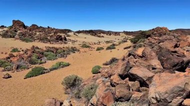 Büyüleyici bir panoramik manzara kayalık arazi ve açık mavi gökyüzünün yer aldığı engin bir çöl manzarasının güzelliğini yakalar.
