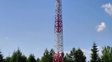 Yeşillik ve açık mavi gökyüzü tarafından çerçevelenmiş yüksek bir iletişim kulesinin çarpıcı görüntüsü dikkat çekiyor.