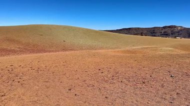 Açık mavi gökyüzünün altındaki renkli yuvarlanan tepelerin nefes kesici manzarası, etrafındaki doğal güzellikleri gözler önüne seriyor.