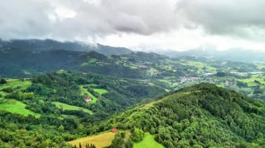 Sarsılan tepeleri ve çarpıcı bulutlu gökyüzünün altındaki canlı yemyeşil alanları gösteren nefes kesici bir hava manzarası.