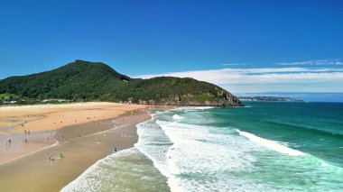 Nefes kesici manzara, yumuşak, dalgalı ve çekici bir tepe arkaplanı olan sakin bir plajdan oluşuyor.