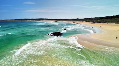 Huzurlu bir kıyı manzarası canlı yeşil sular, yumuşak kumlu plajlar ve engebeli kaya çıkıntıları sergiliyor.