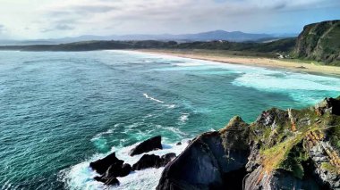 Uçurumları, kumlu sahili ve dalgalı okyanus dalgalarını güzellikle gösteren çarpıcı bir kıyı manzarası.