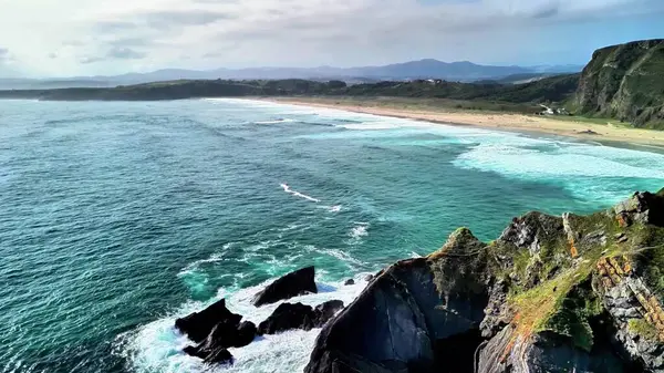Uçurumları, kumlu sahili ve dalgalı okyanus dalgalarını güzellikle gösteren çarpıcı bir kıyı manzarası.