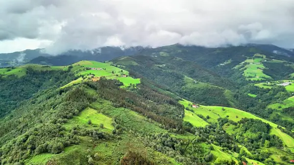 Göz kamaştırıcı bir hava manzarası yemyeşil dağları ve yuvarlanan tepeleri sergiliyor bulutlu bir gökyüzünün altında.