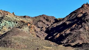 Berrak mavi gökyüzüne karşı canlı kaya dokularıyla engebeli dağların nefes kesici manzarasının tadını çıkar.