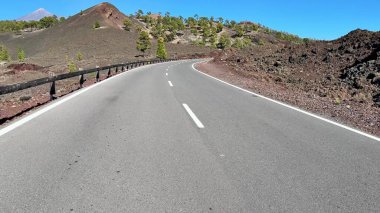 Güzel, dolambaçlı bir yol, yukarıdaki açık mavi gökyüzünün altında sersemletici bir volkanik arazide zarifçe ilerliyor.