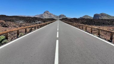 Büyüleyici volkanik bir arazide, arka planda görkemli dağlar bulunan çarpıcı bir yol esiyor.