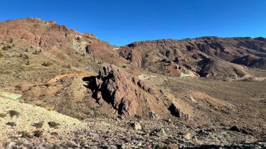 Kurak arazinin nefes kesen manzarası berrak mavi gökyüzünün altında kayalık oluşumları sergiliyor.