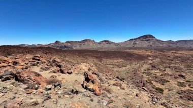Geniş ve nefes kesici çöl arazisi, açık güneşli bir gökyüzünün altında kayalık oluşumlar ve görkemli dağları barındırır.