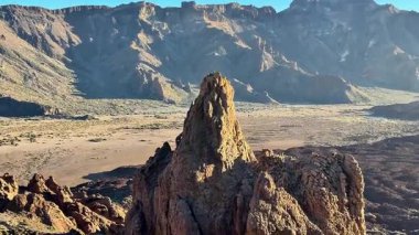 Tamamen çarpıcı bir kaya oluşumu engin çöl arazisiyle güzelce çerçevelenmiş, hepsi açık mavi bir gökyüzünün altında.