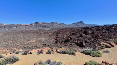 Uçsuz bucaksız bir çöl manzarasını, berrak mavi gökyüzünün altındaki kayalık dağları deneyin.