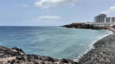Kıyı sahili, kayalık bir sahil ve berrak mavi gökyüzünün altında ışıl ışıl deniz kenarında büyüleyici bir otel.