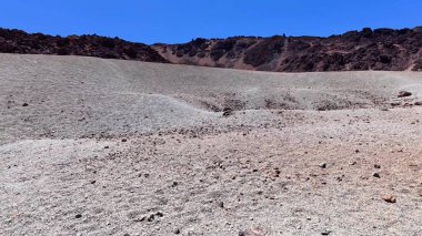 Açık mavi gökyüzünün altında uzanan engebeli ve çorak bir arazi, doğal temalı projeler için ideal hale getiriyor.